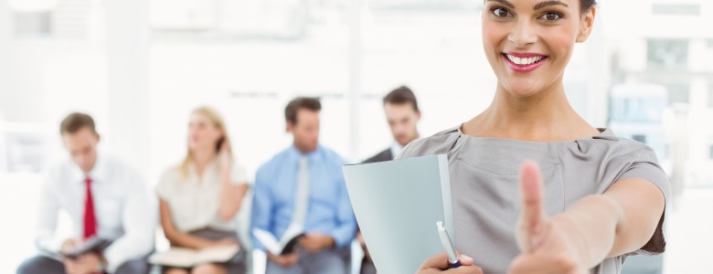 Businesswoman gesturing thumbs up against people waiting for interview