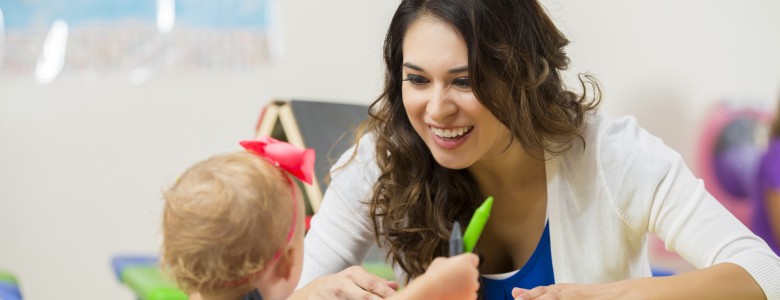 Pretty daycare teacher helps toddler with coloring project